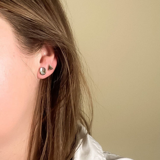 Close-up of a person wearing a triangle and oval-shaped earring against a beige background