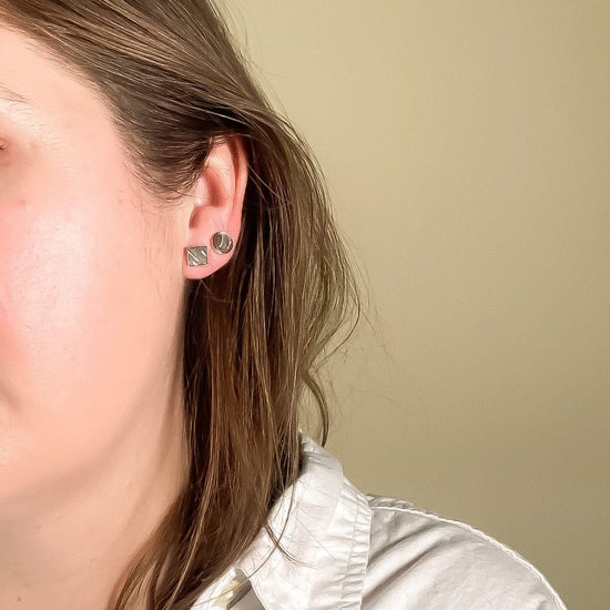 Person wearing abalone square and circle stud earrings with a neutral background